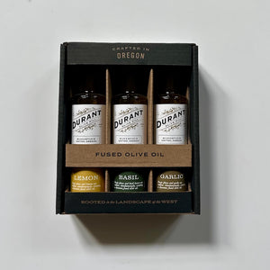 Box of 3 Durant fused olive oil bottles with labels for lemon, basil, and garlic on a light gray background.