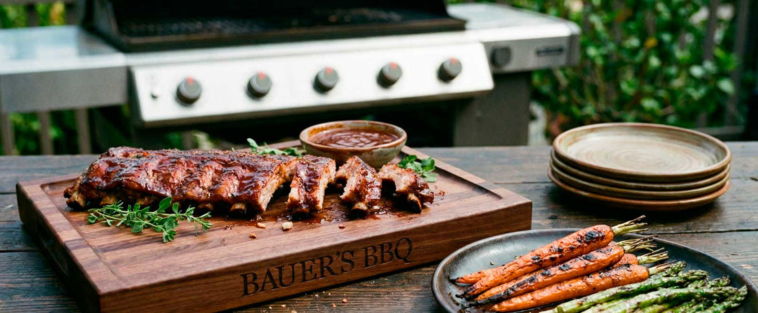 BBQ meat board personalized with name and shown with spare ribs and roasted carrots and asparagus on table outdoors with grill in background