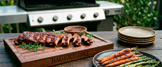 BBQ meat board personalized with name and shown with spare ribs and roasted carrots and asparagus on table outdoors with grill in background
