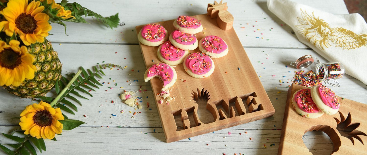 small maple rectangle board with HOME cut out of the wood and the O is a pineapple shape, shown with pick iced cookies on white wood 