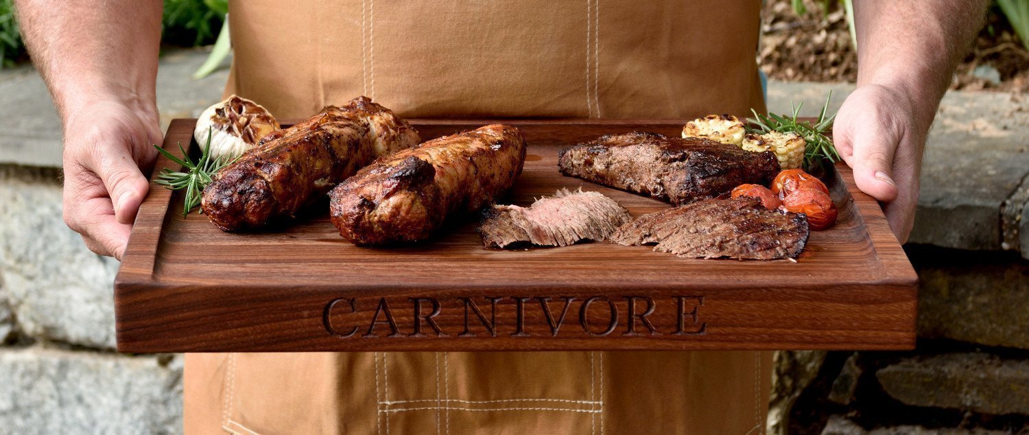 Man holding walnut meat board with slope, grilled steak and chicken on board 