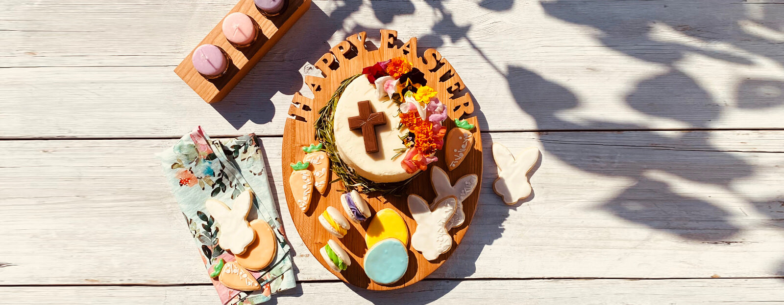 Easter egg shaped cutting board with easter cake and cookies on white wood bacground