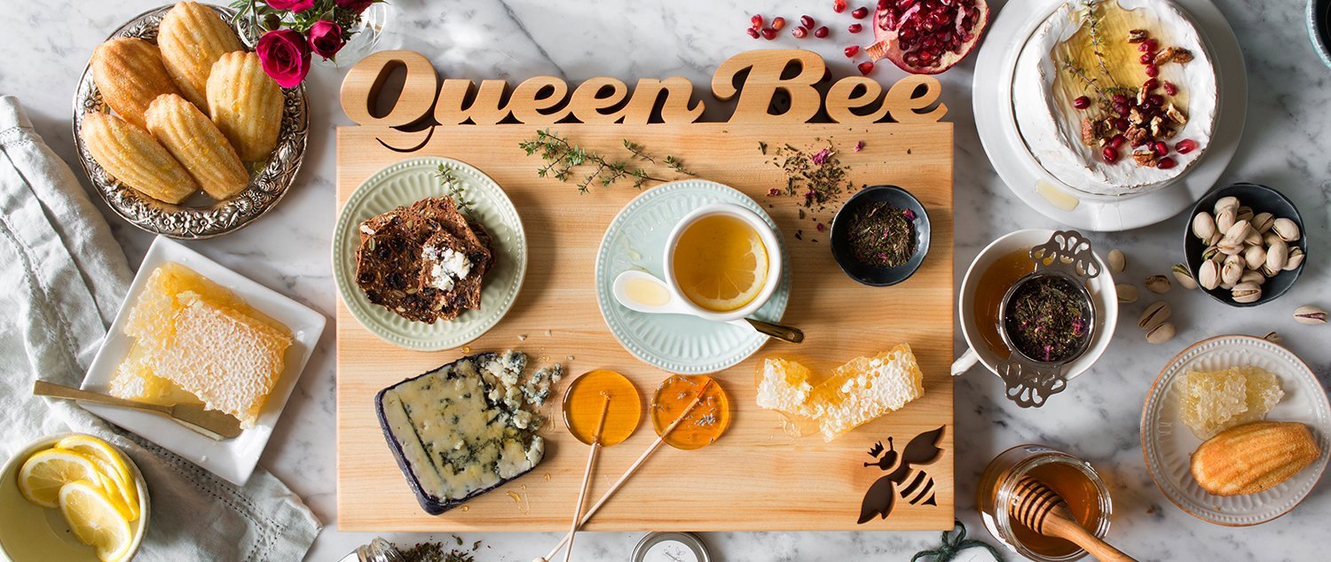 Rectangle maple board with 'Queen Bee' cut out of the top, tea and biscuits on marble background