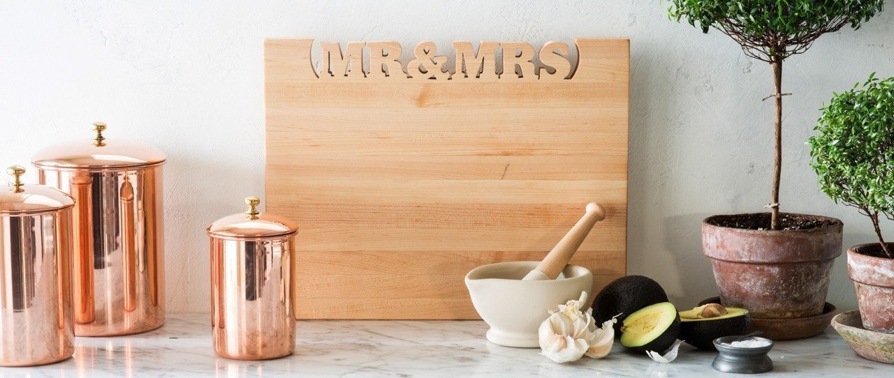 maple rectsngle cutting board with 'mr & mrs' cut out of the top, sitting against backsplash 