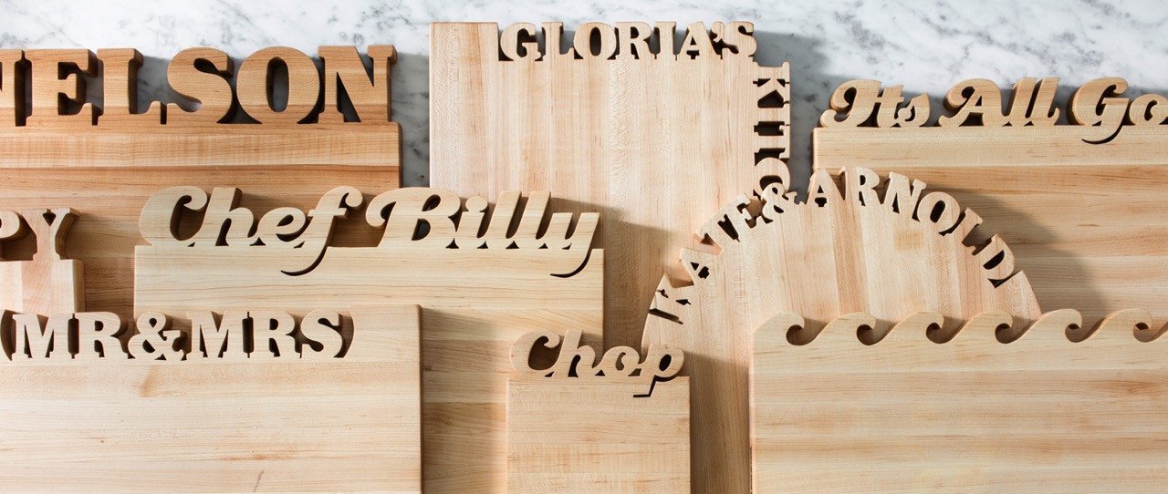 A collection of personalized maple cutting boards with names cut out of the top, marble background