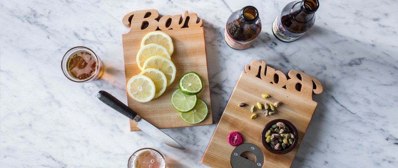 mini maple boards with the word Bar cut out of the wood, shown with cut lemons and limes on marble counter