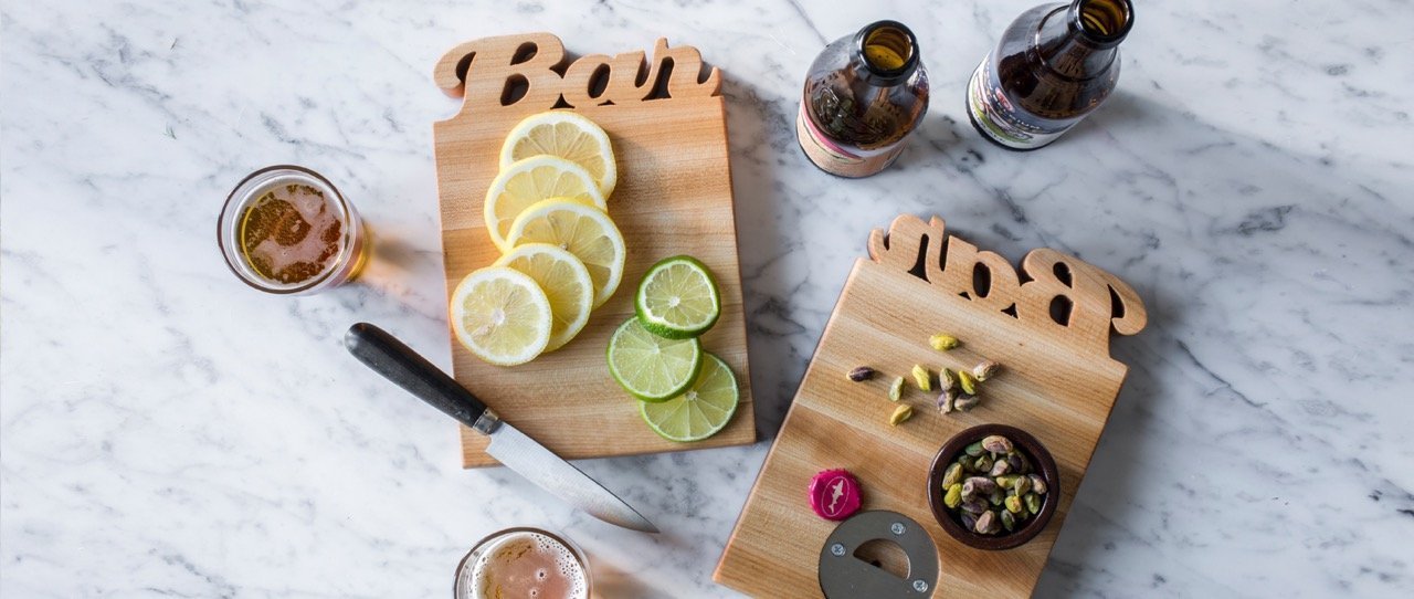 small maple board with 'Bar' cut out of the top of the wood, cut lemons, limes and pistachios on board, on marble counter