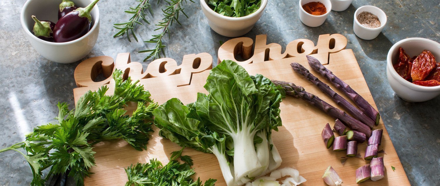 rectangular wooden chopping board with the words "chop chop" carved above the board. Plenty of vegetables on the board