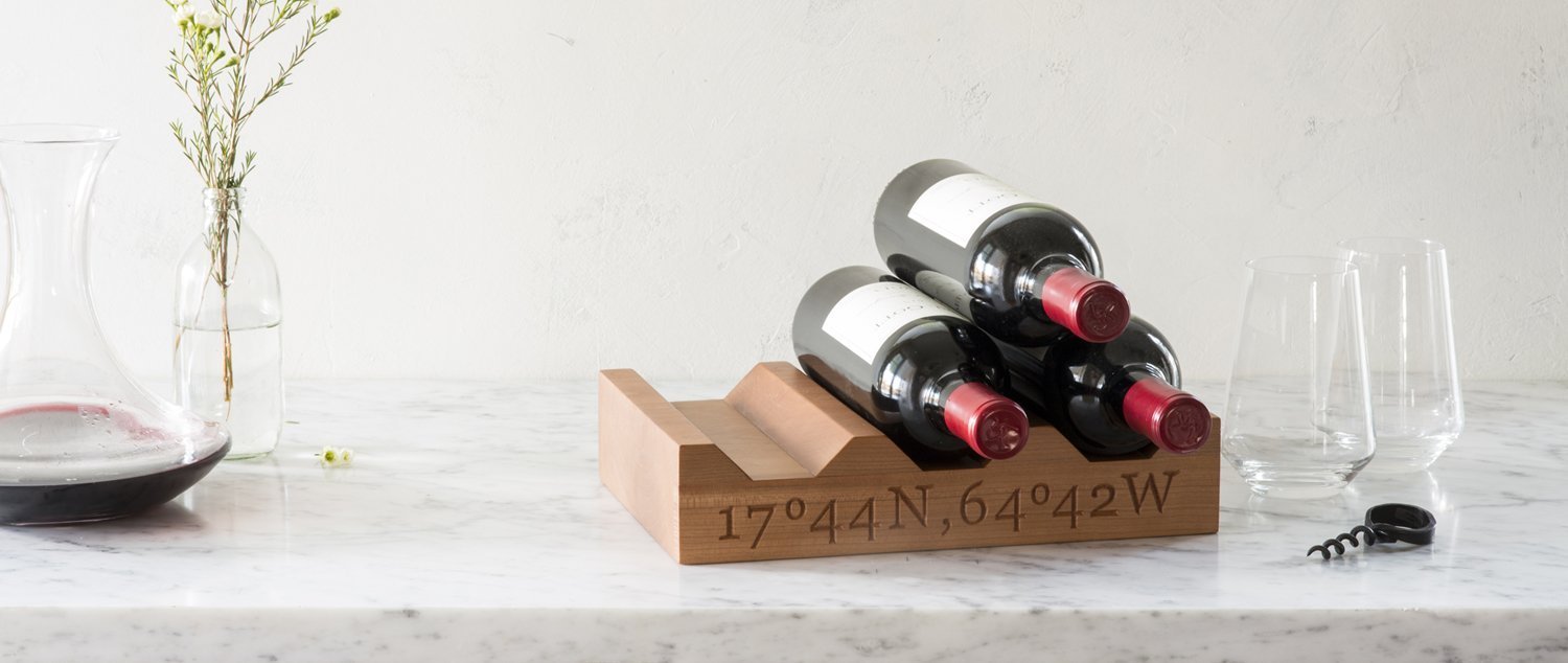 cherry wood wine racks holding 3 bottles of wine, on marble counter with 2 wine glasses