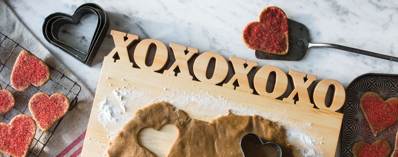 cutting board with the letters XOXOXOXO cut out of the top with heart shaped cookies on marble counter