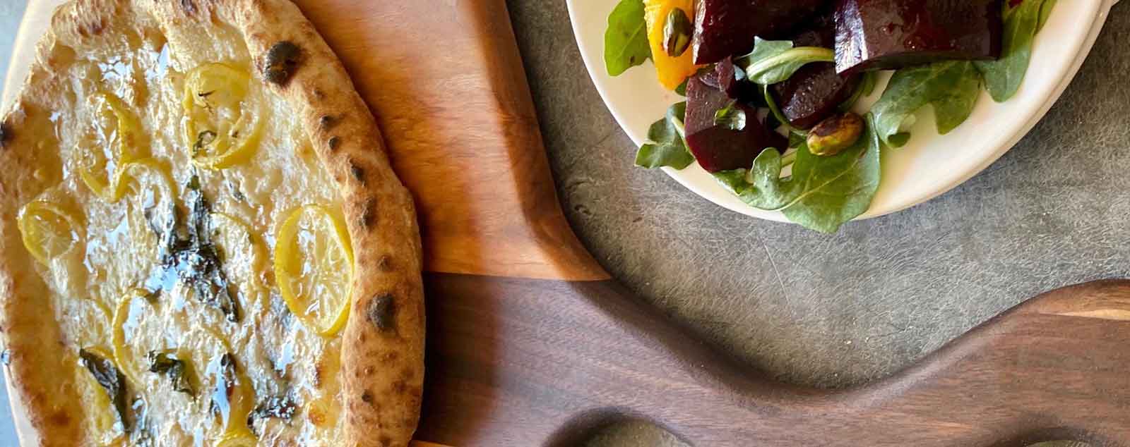 wooden pizza peel - cherry and walnut with lemon pizza on top and salad on counter