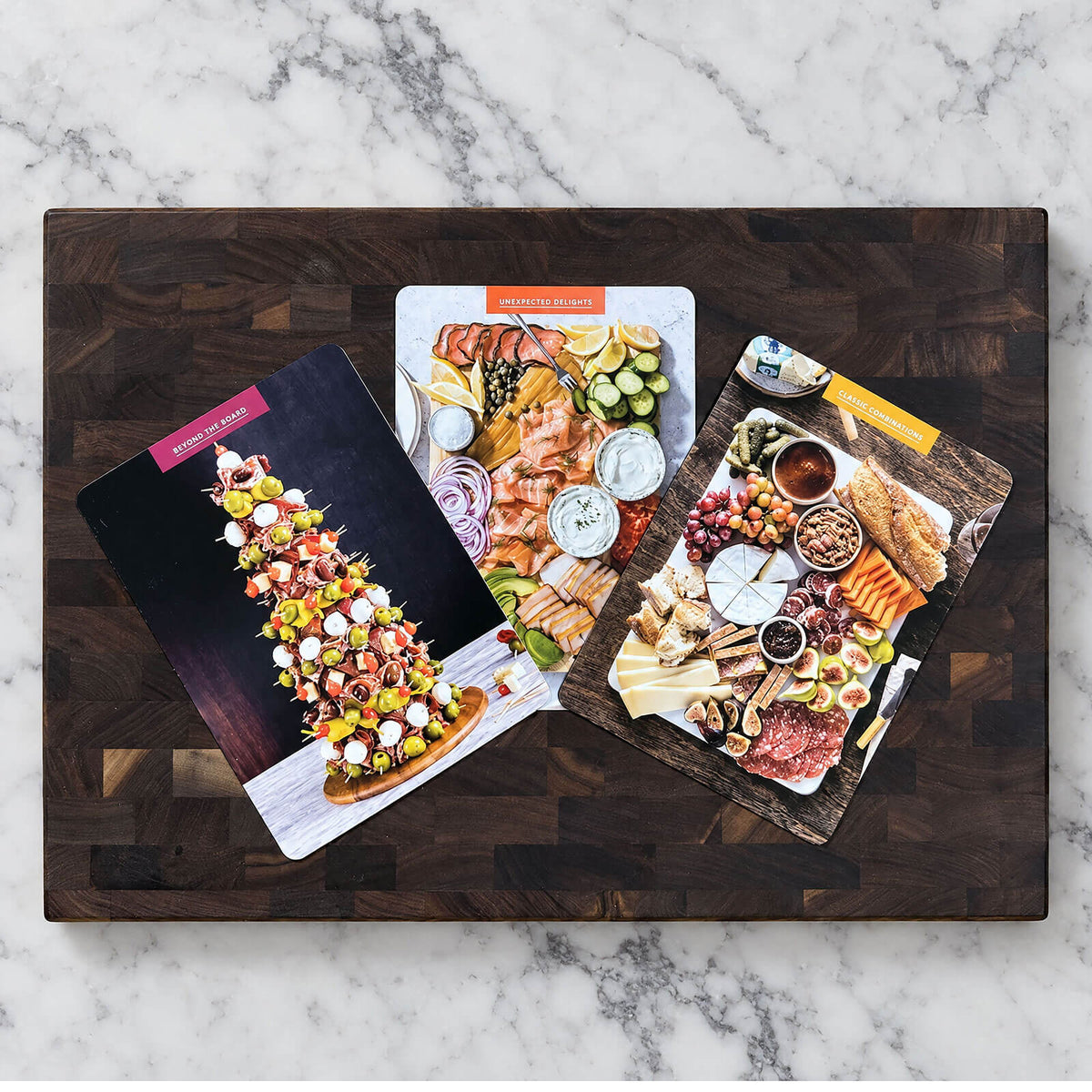 front of 3 cards from The Charcuterie board deck sitting on cutting board, on marble counter