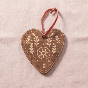 Wooden heart-shaped ornament with floral patterns and a red velvet string on a pink background
