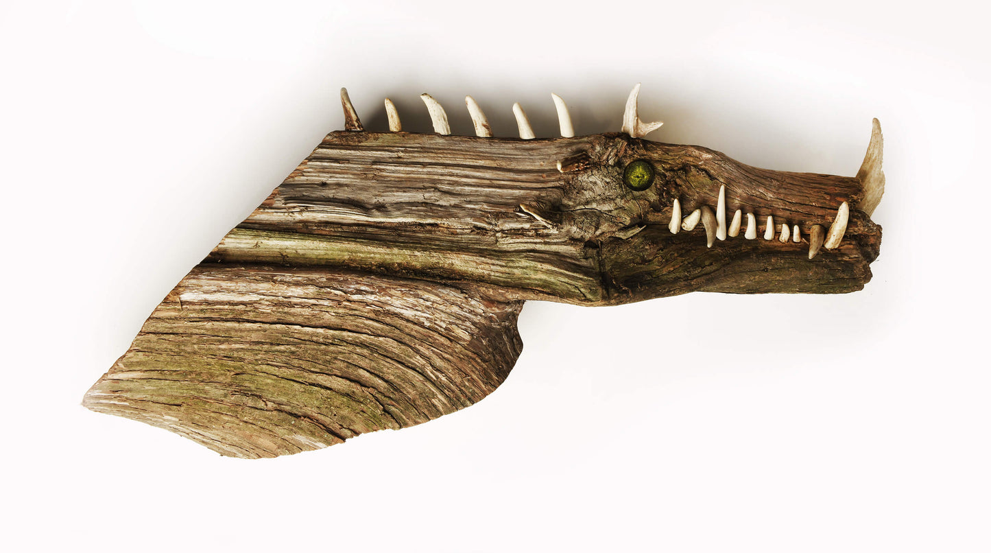 A wooden sculpture depicting a fantastical creature with a combination of naturalistic elements and fantastical features, such as a dragon's head with teeth and eyes added to a piece of juniper tree.