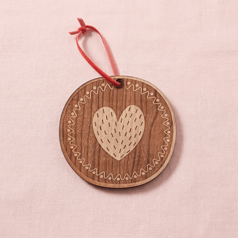 Wooden 'O' ornament with a heart design and red string on a pink background