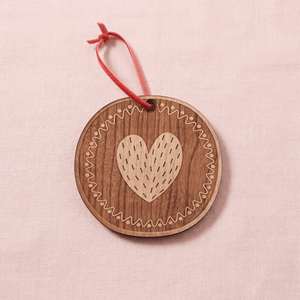 Wooden 'O' ornament with a heart design and red string on a pink background