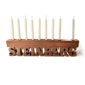 Wooden menorah with 'Steinberg' engraving and unlit candles on a white background