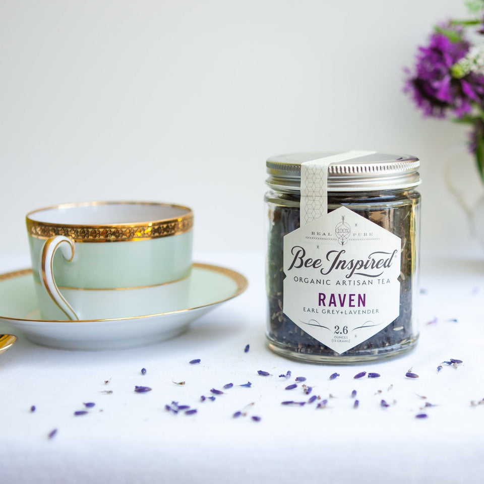 purple loose tea in glass jar sitting on white counter with tea cup and saucer