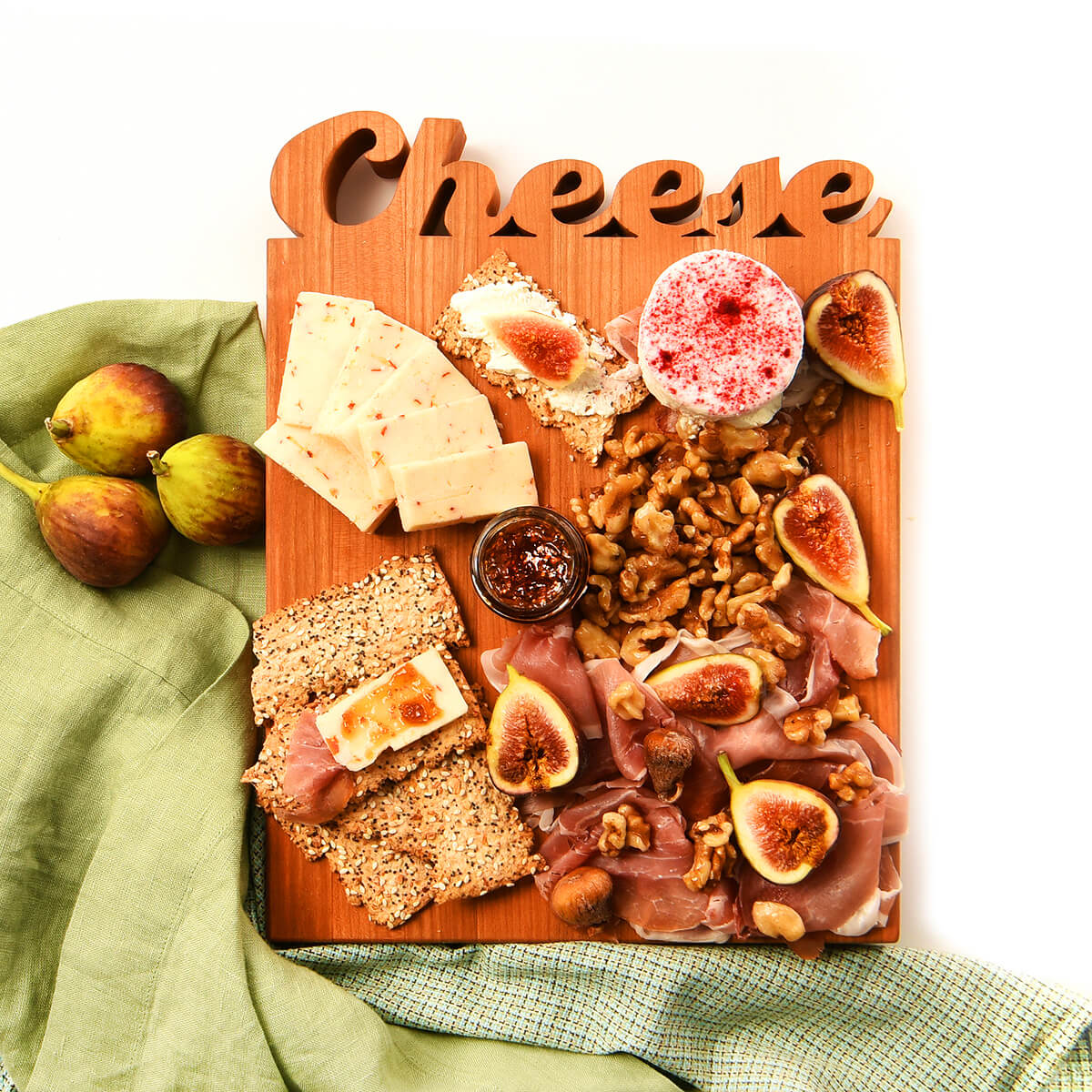 Wooden cheese board with assorted cheeses, figs, and meats on a green napkin.