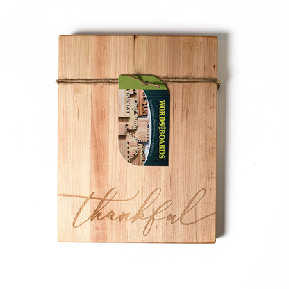 A rectangular maple wood cutting board with 'Thankful' laser engraved in cursive script, tied with a string and a tag.