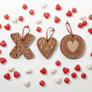 1 X shaped ornament, 1 O shaped ornament and 1 heart shaped ornament with red hang tie on white background with red and white heart and round candies