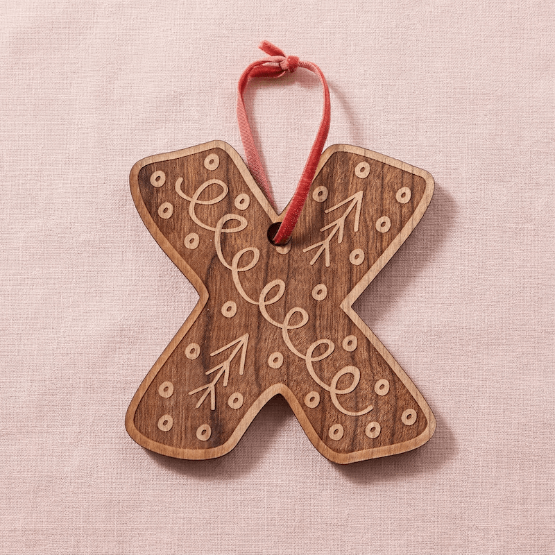 Wooden letter 'X' ornament with decorative Scandinavian design on a pink background