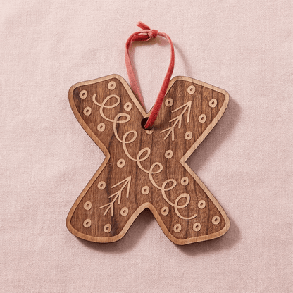 Wooden letter 'X' ornament with decorative Scandinavian design on a pink background