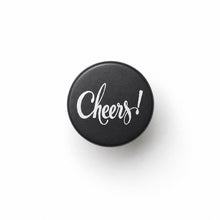 black metal bottle stopper with Cheers! engraved on top, white background