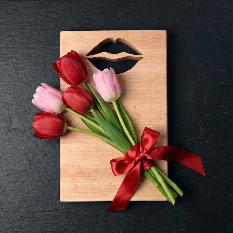 Wooden board with lips cut out of the top with red and pink tulips tied with a red ribbon on a dark background