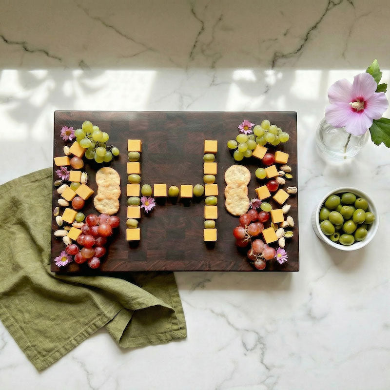 end grain cutting board with fruit and cheese arranged in a decorative pattern on a marble surface.
