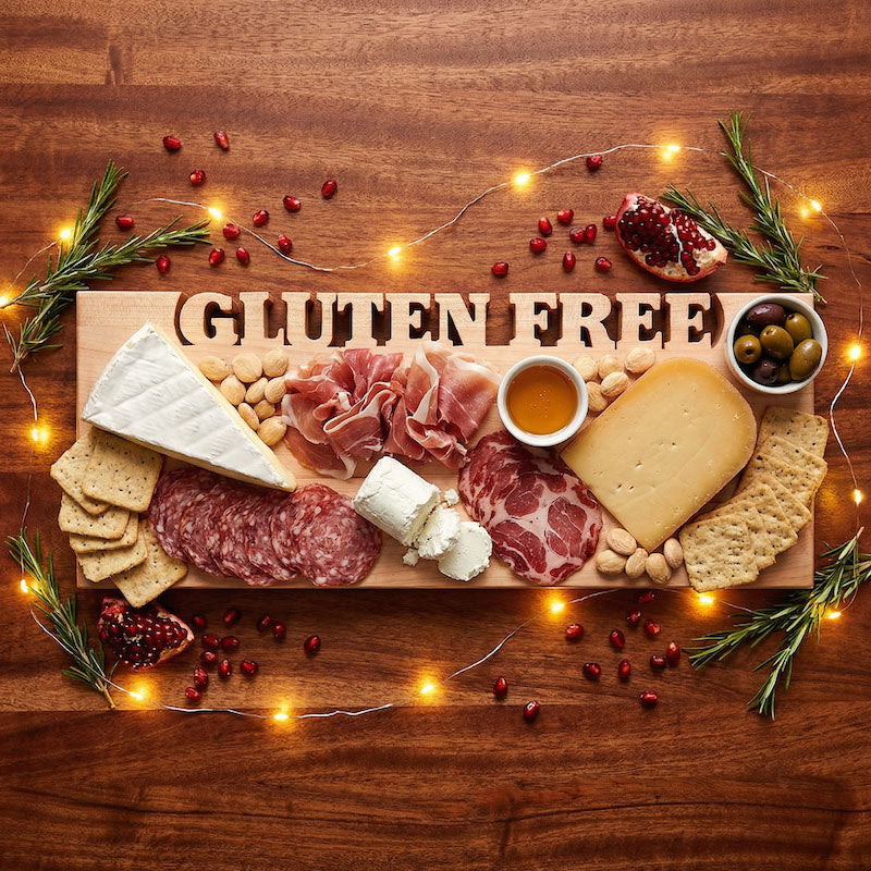 Gluten-free serving board topped with charcuterie, 3 cheeses, and crackers on a wooden surface with string lights