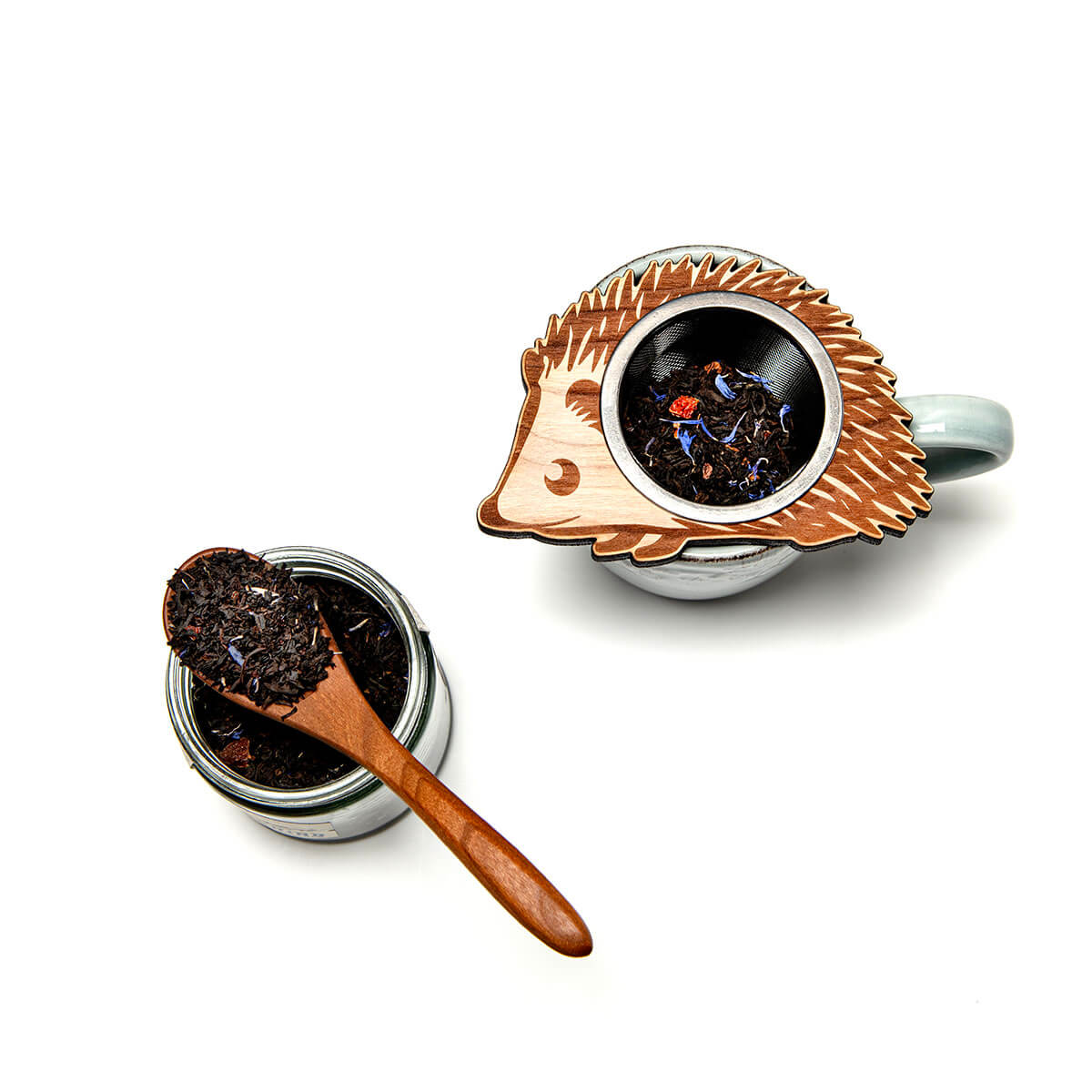 Hedgehog-shaped tea infuser with a small container of loose tea and a wooden spoon on a white background