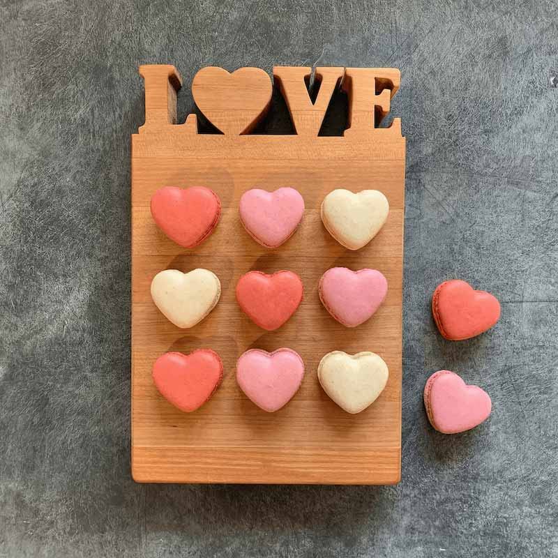 Heart-shaped macrons on a wooden board with 'LOVE' letters on a gray background