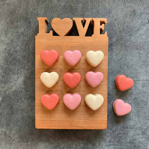 Heart-shaped macrons on a wooden board with 'LOVE' letters on a gray background