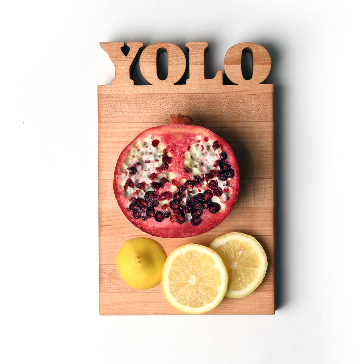 mini cutting board with the letters YOLO cut out, pomegranate and lemons shown on board