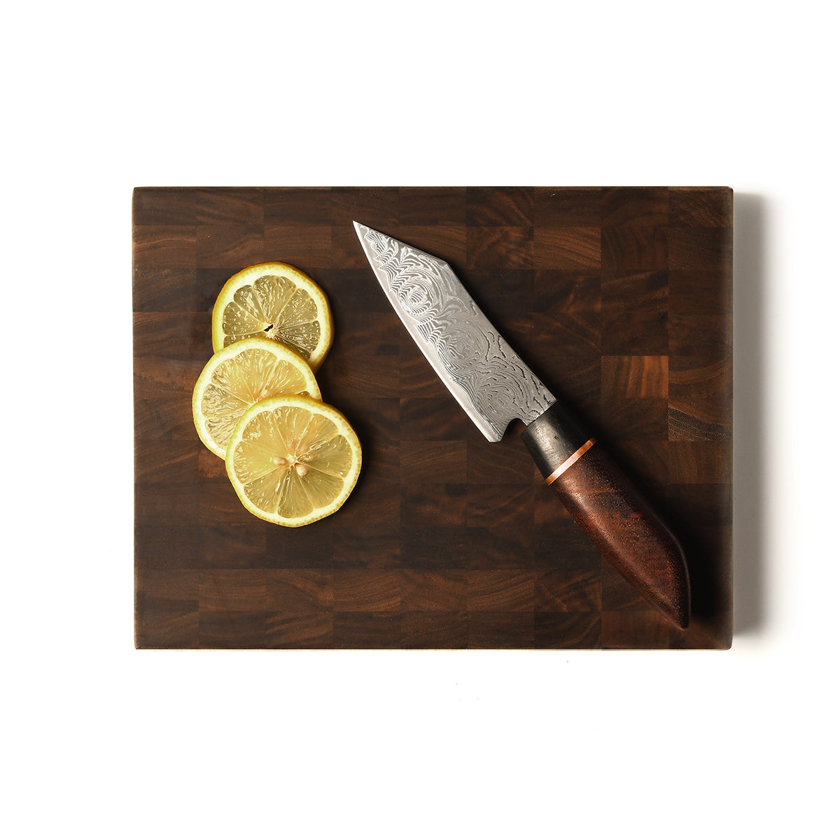 petty knife on end grain board with lemons on white background