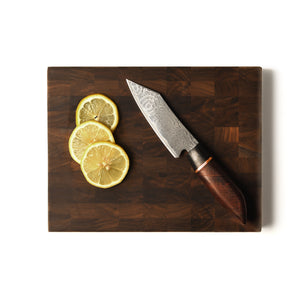 petty knife on end grain board with lemons on white background