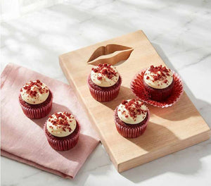 Red velvet cupcakes with cream cheese frosting on a wooden board with lip shape cut out and pink napkin.