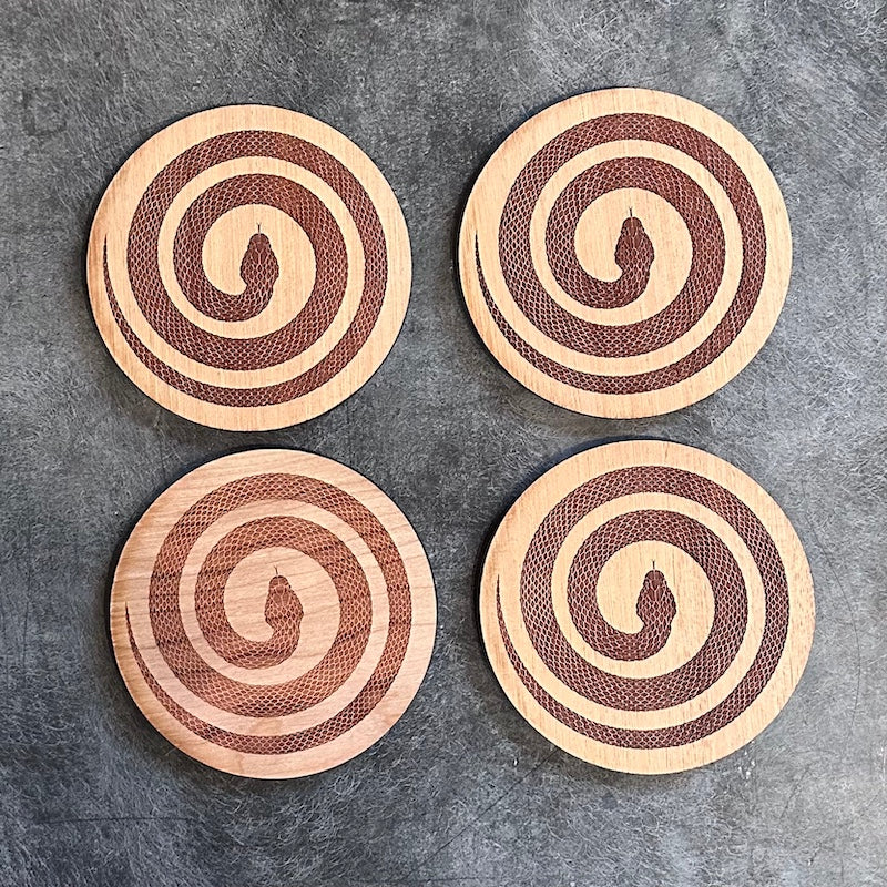 Four wooden coasters with a snake in a spiral pattern on a gray surface
