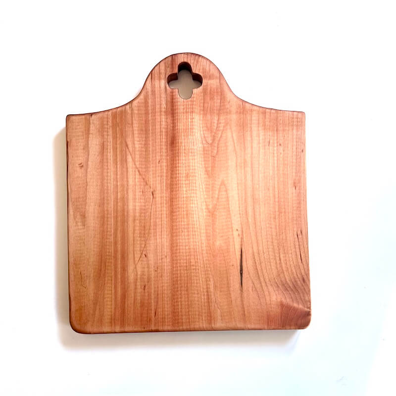 Wooden cutting board with a 4 petal flower-shaped hole on a white background