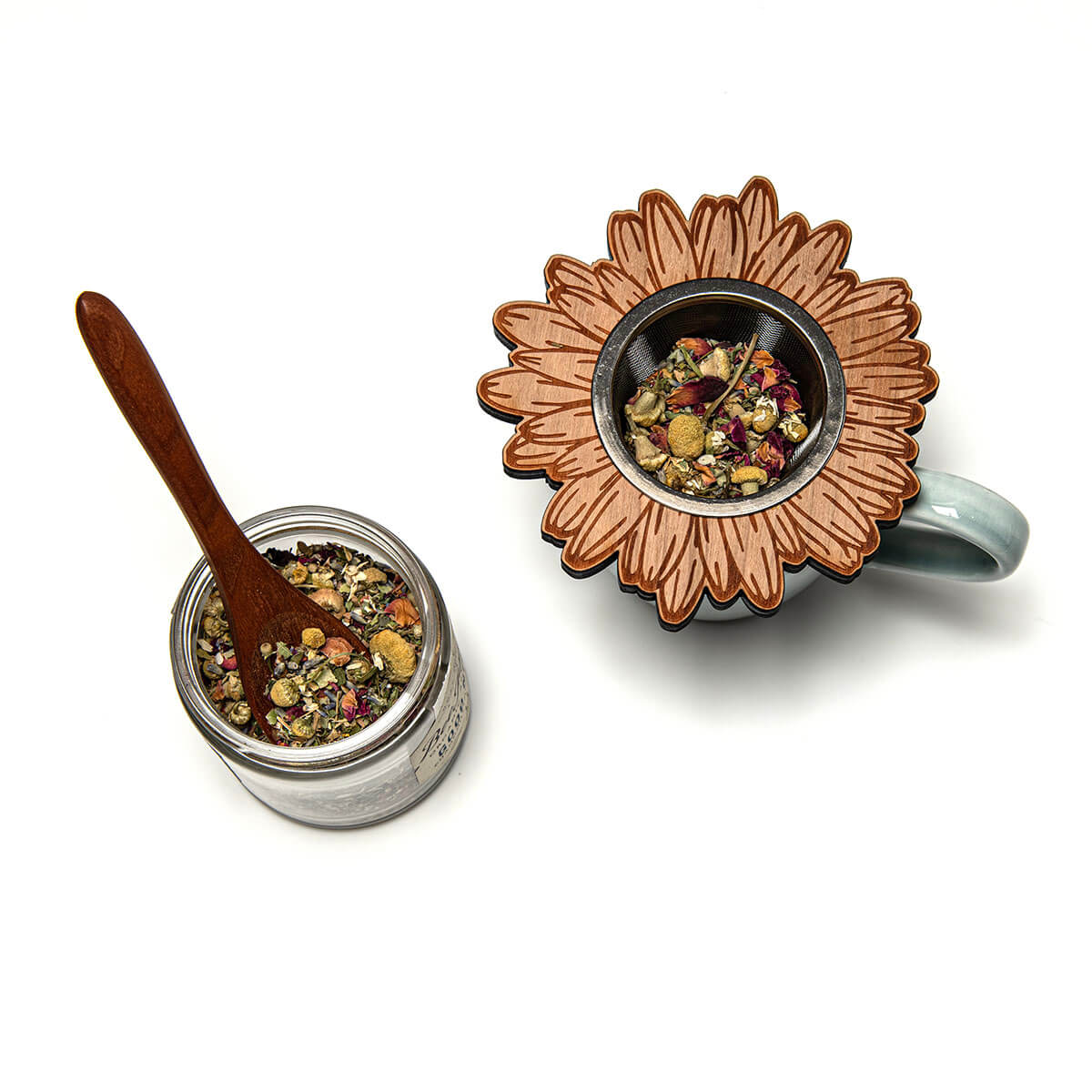 Tea jar with wooden spoon and sunflower-shaped tea infuser on a white background