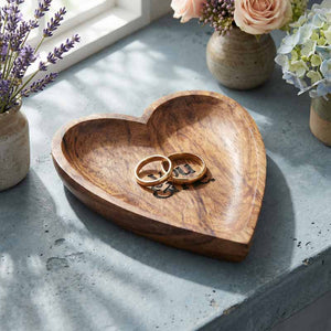 Wooden heart-shaped dish with rings on a concrete surface with flowers in the background