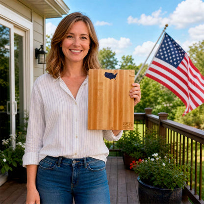 Woman holding a wooden cutting board with a U.S. map design on a deck with an American flag in the background.