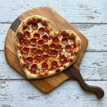 Heart shaped pizza with pepperoni on a wooden pizza peel