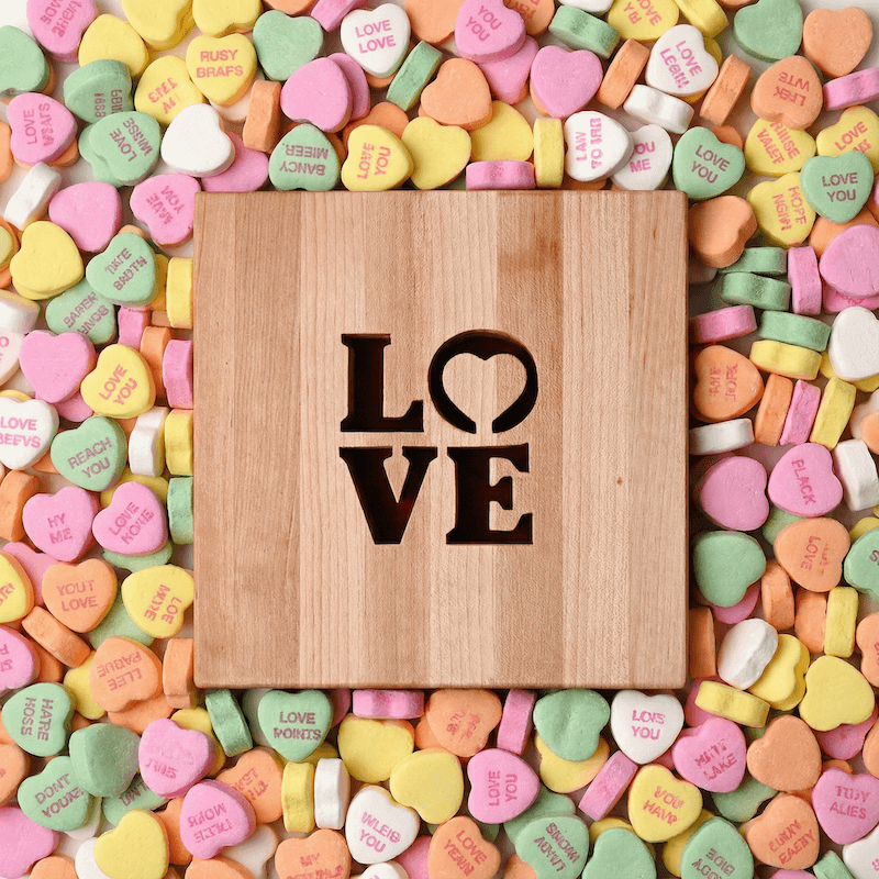 Wooden trivet with 'LOVE' cut out surrounded by colorful heart-shaped candies.