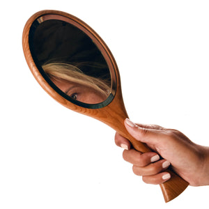 Wooden hand mirror, someone holding the mirror in hand and looking into mirror
