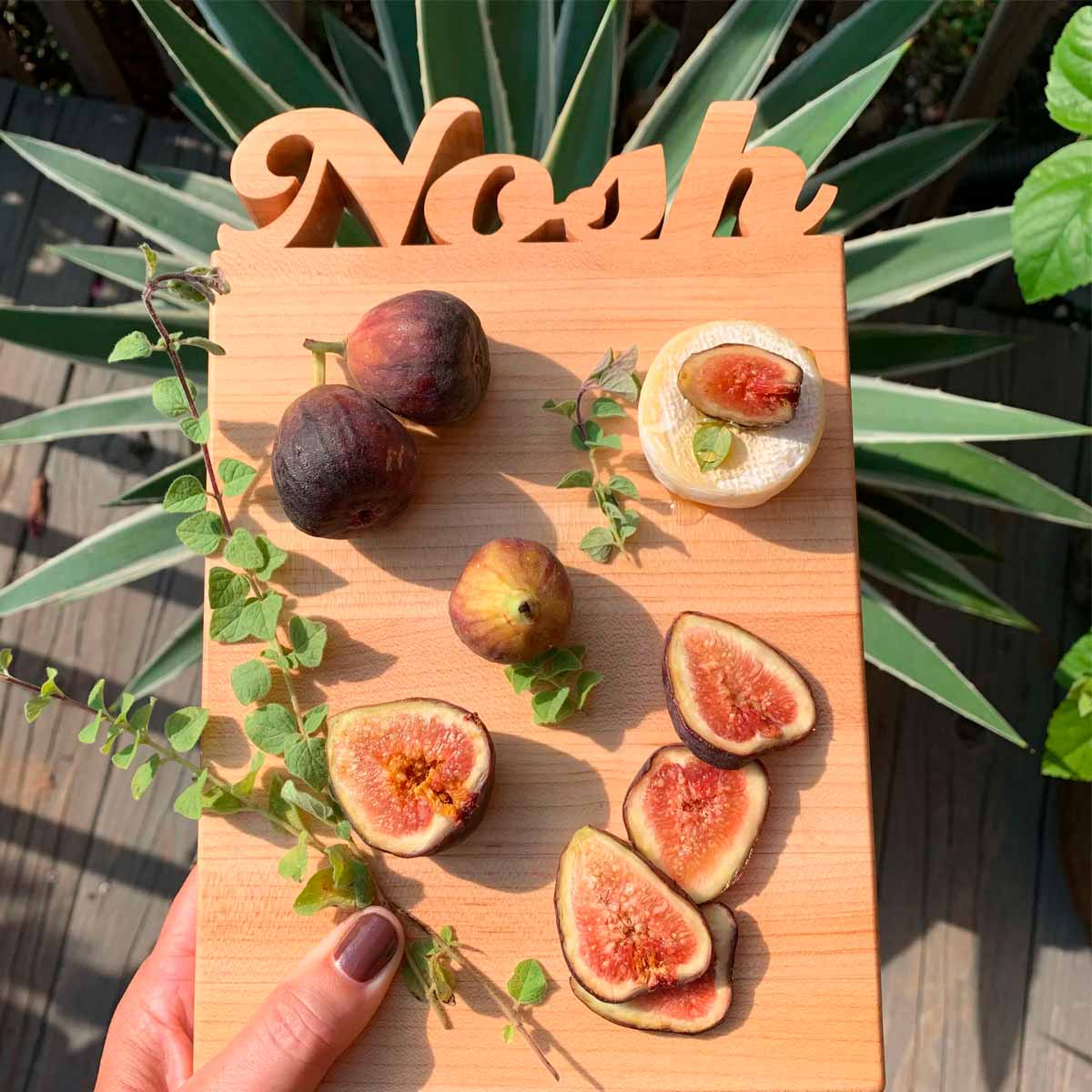 Cutting board with the work Nosh cut out of the wood - shown this figs and cheese